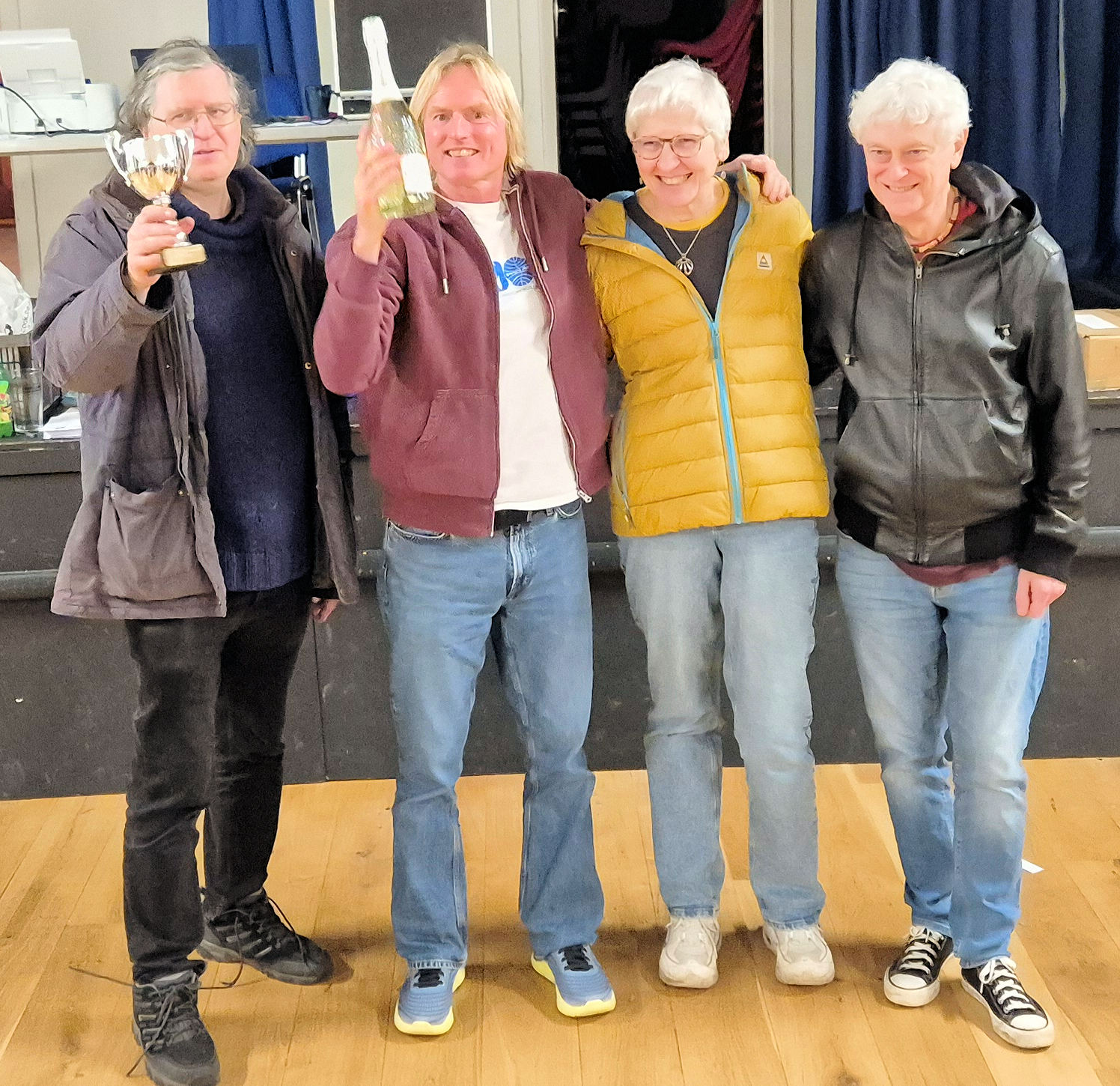 4 people standing with a trophy and bottle of wine